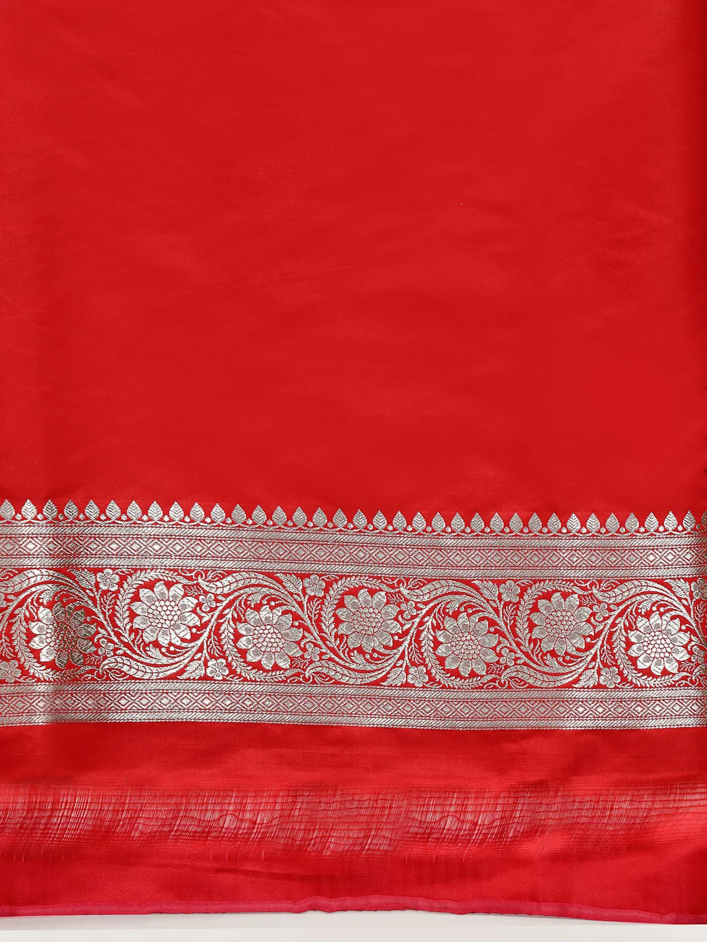 A close-up of a bright red fabric, likely silk or satin, featuring a wide decorative border with intricate silver metallic floral and scrollwork patterns.